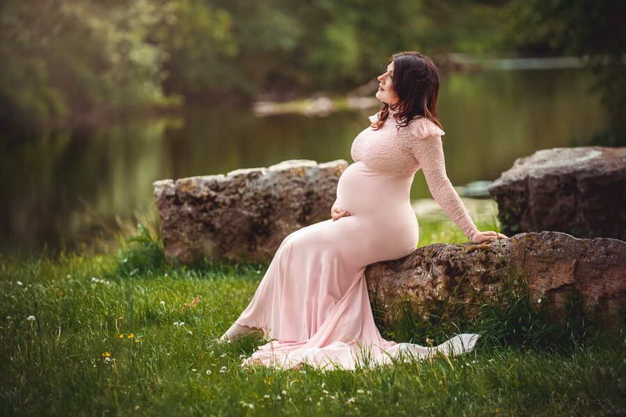 eine Schwangere Frau im rosafarbenen Kleid sitzt auf einem Stein