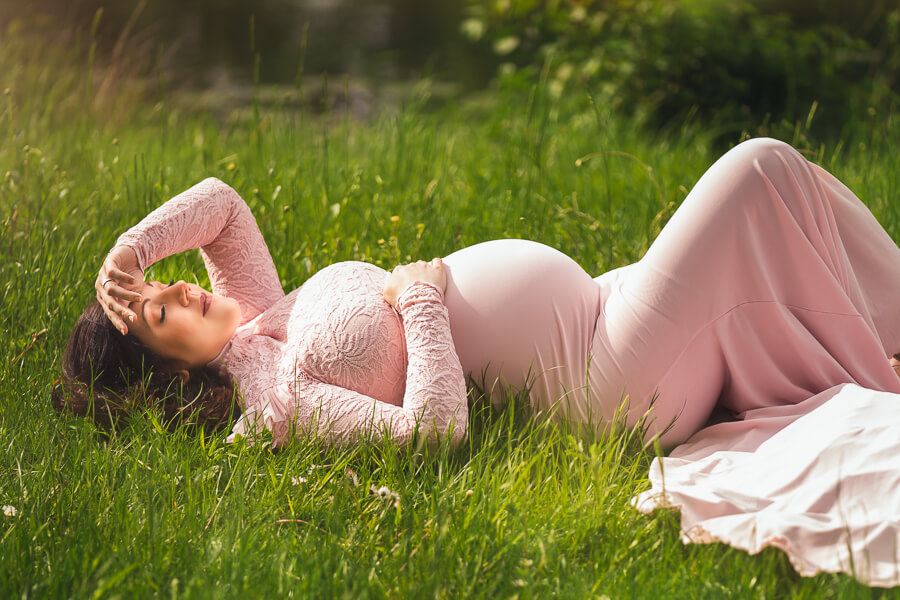 Eine Schwangere Frau im rosafarbenen Kleid liegt im Gras