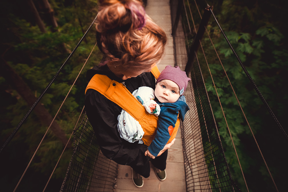 Eine Mutter hat ihr Kind in der Trage und steht auf einer Hängebrücke